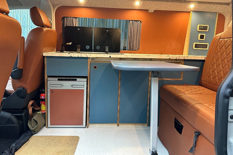 blue and orange furniture inside a converted van. Shows the kitchen and leather seats.