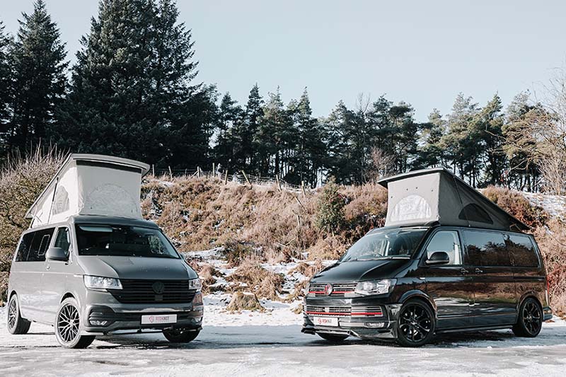 Two Volkswagen campervans facing each other with the pop-tops open in a forest setting