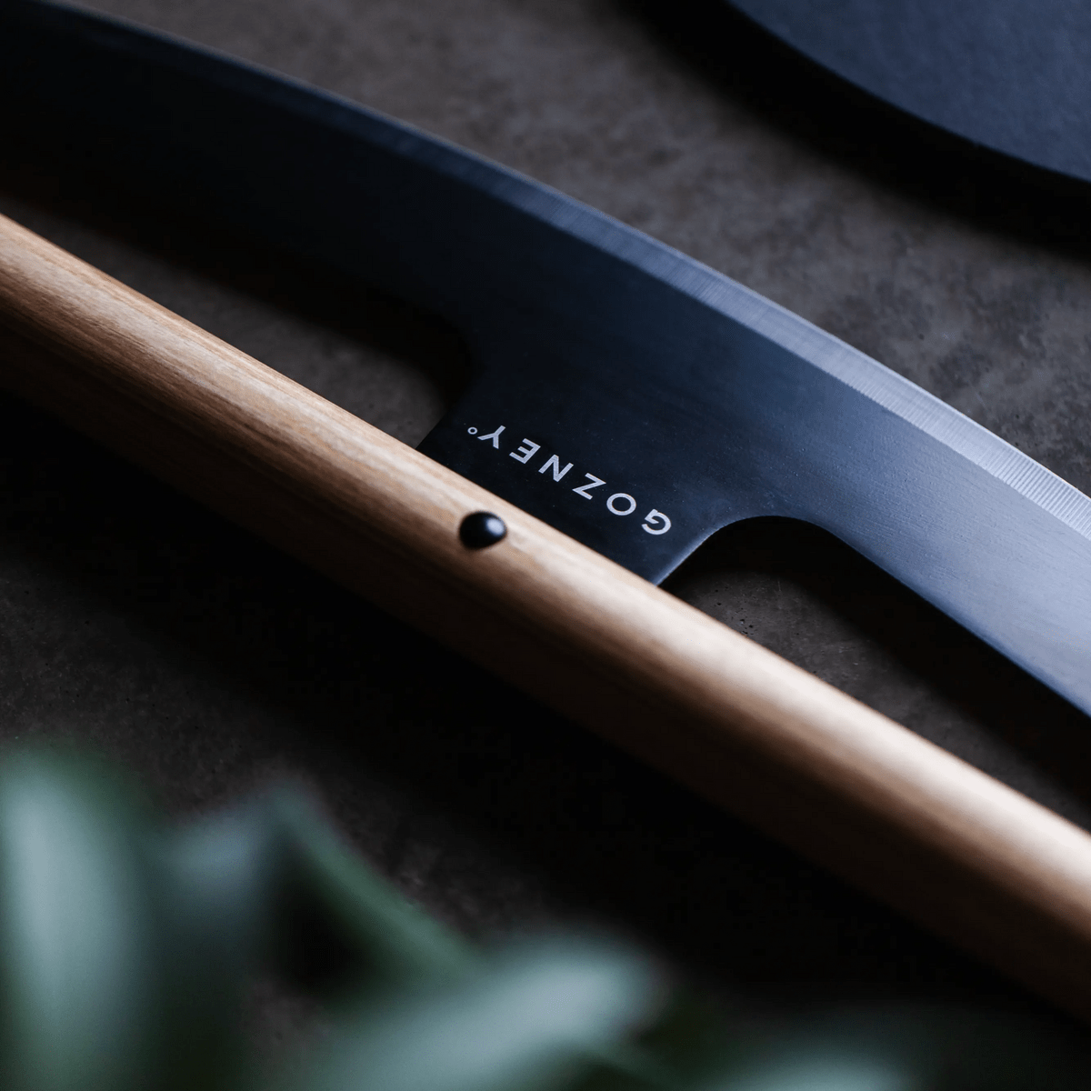 Gozney Pizza Rocker with a dark stainless steel blade and light wooden handle, featuring the brand logo.