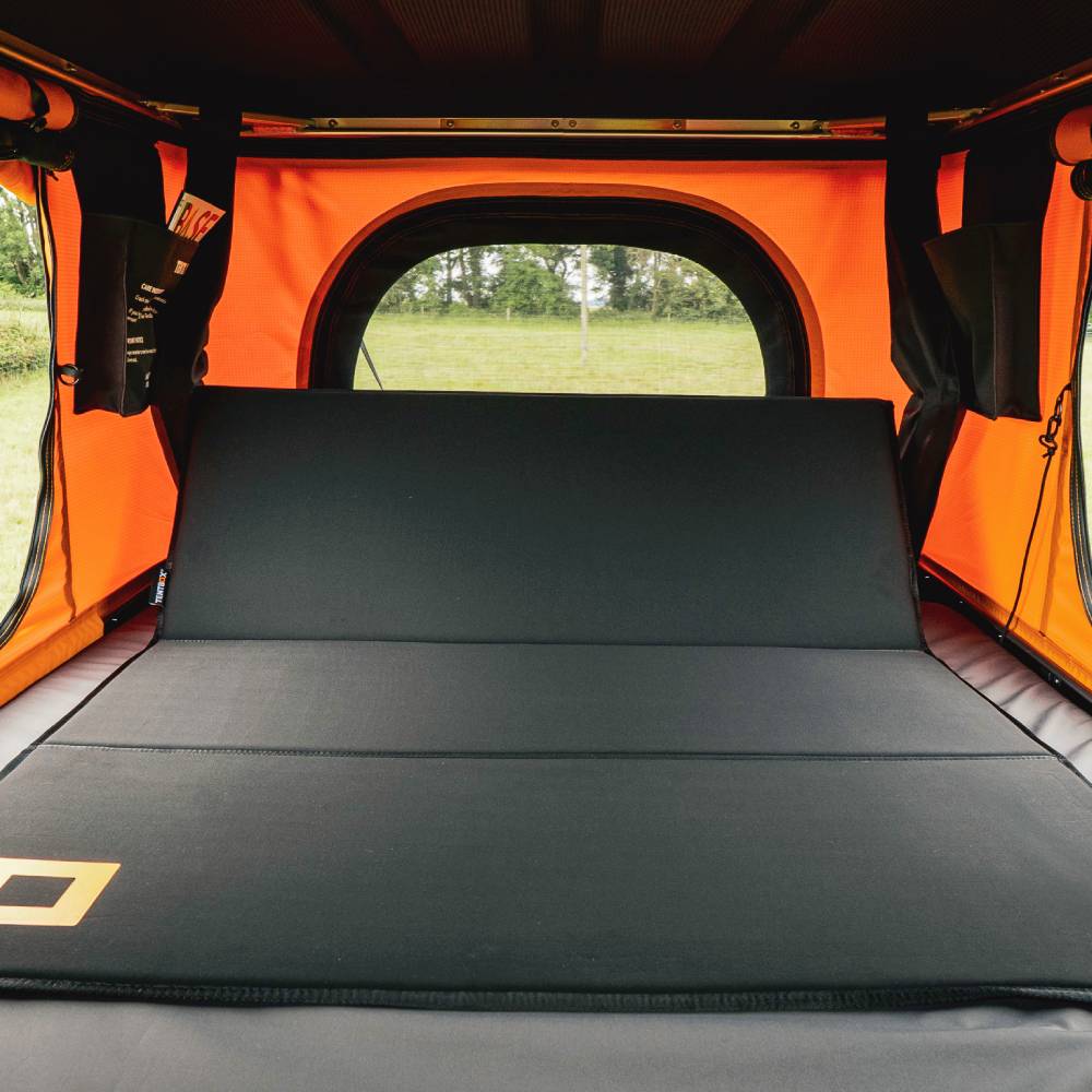 Black TentBox Back Rest with premium padding, clipped to an orange roof tent, overlooking a green field.