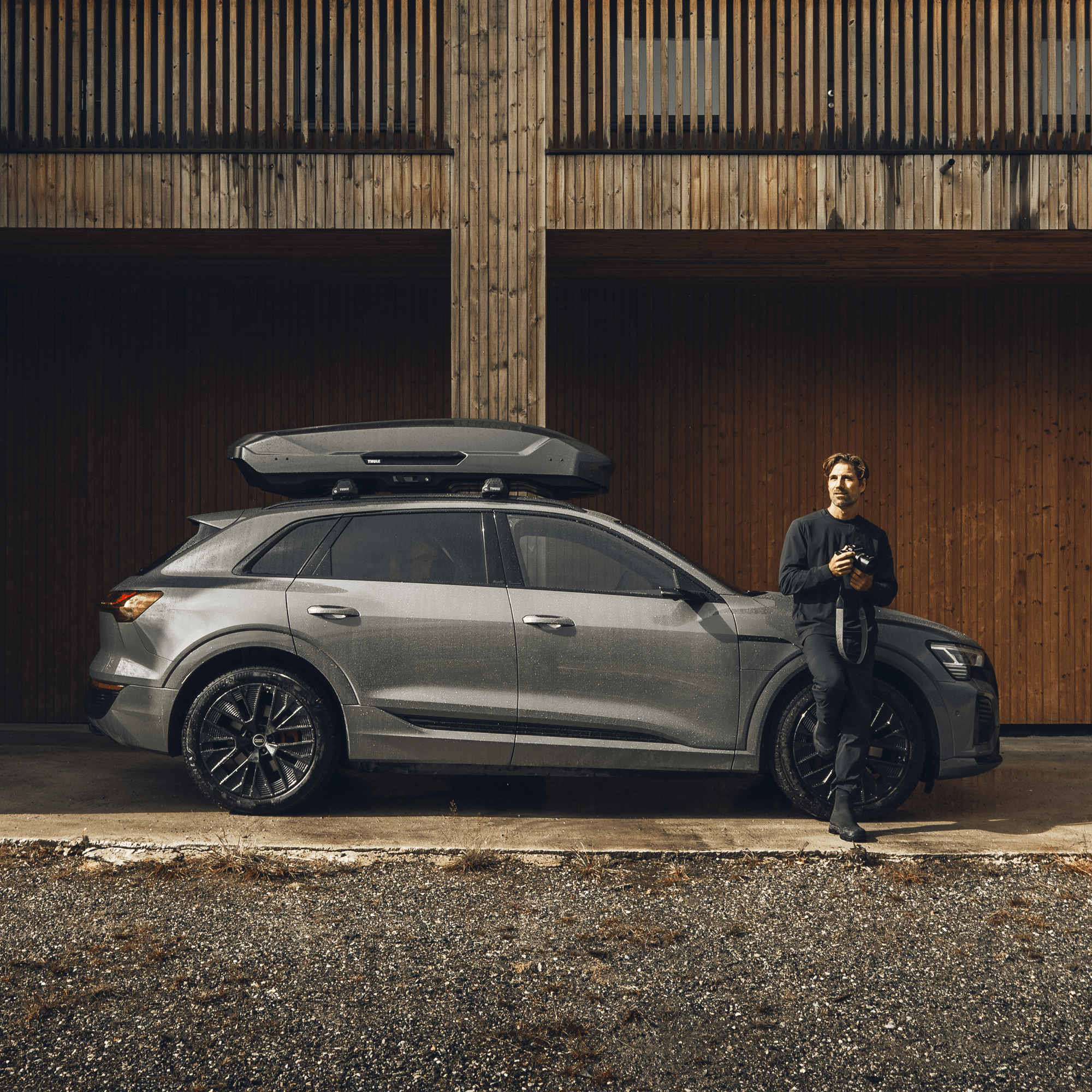 Glossy black Thule Motion 3 L roof box on a gray SUV, with a man leaning against the car.