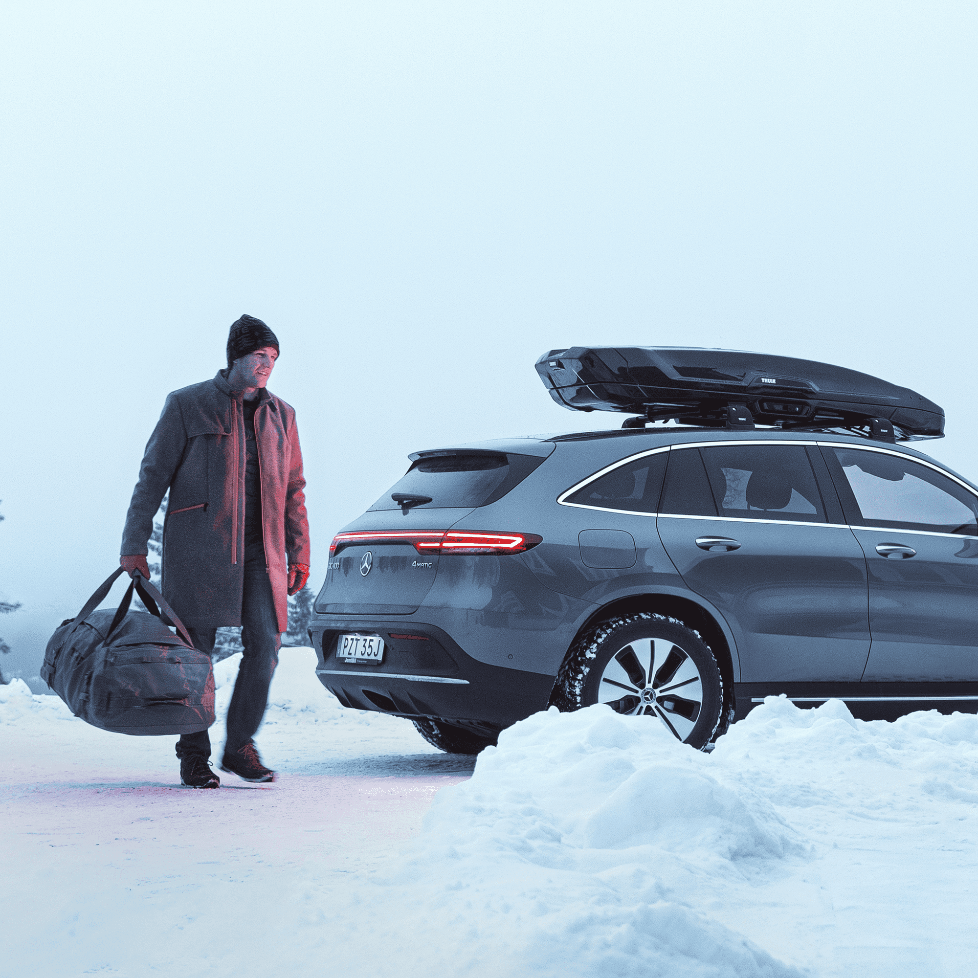 Thule Vector L black metallic roof box on a gray SUV in a snowy landscape.