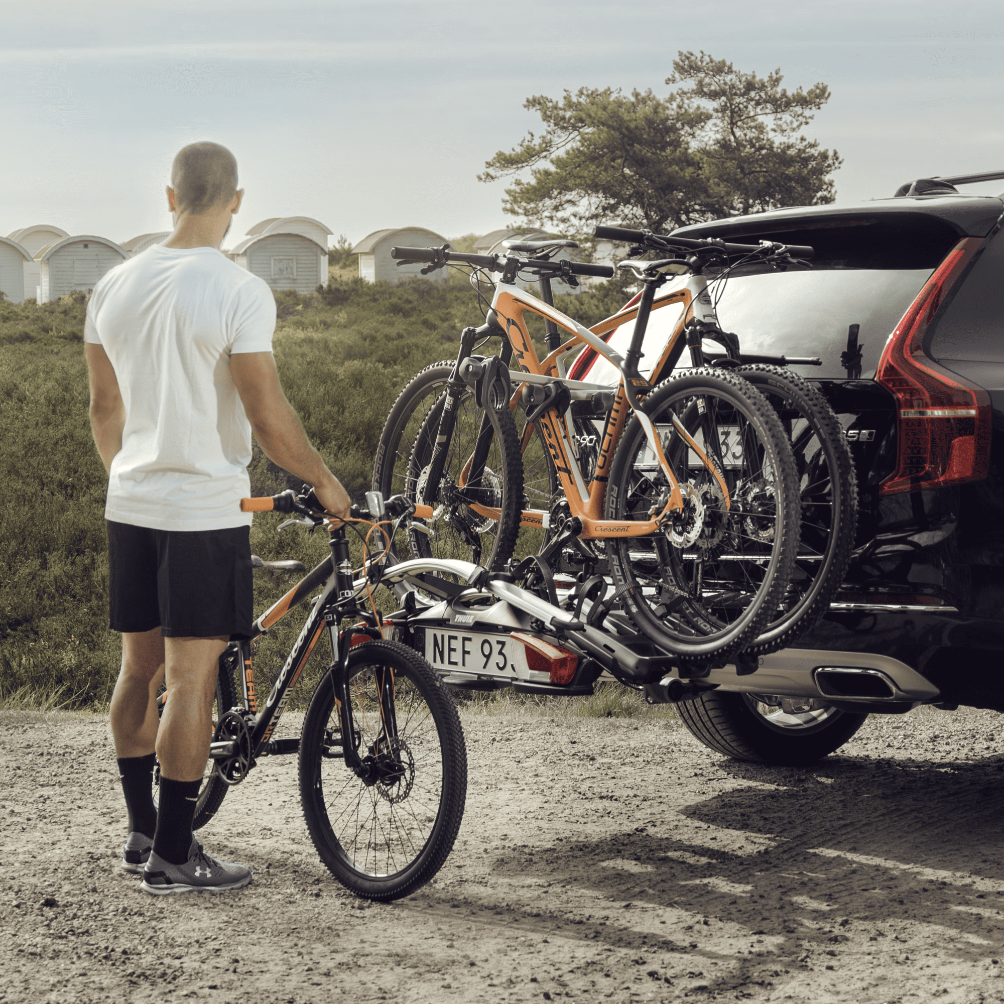 Man loading an orange mountain bike onto a silver Thule VeloCompact 2 bike rack on a black SUV.