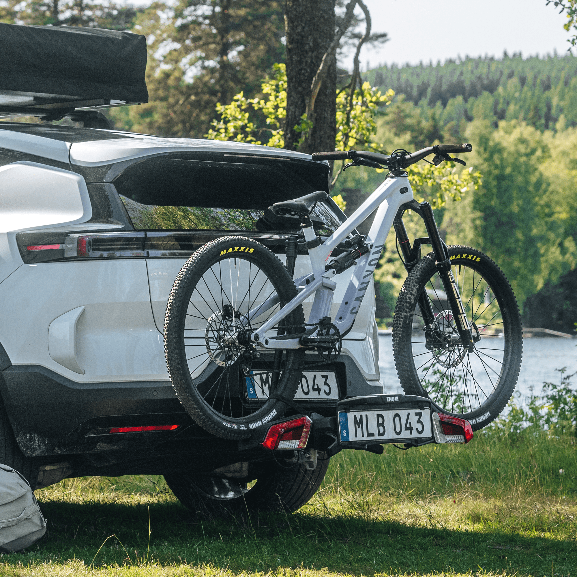 Thule VeloLite 1 black towbar bike carrier mounted on a white SUV, holding a light grey mountain bike.