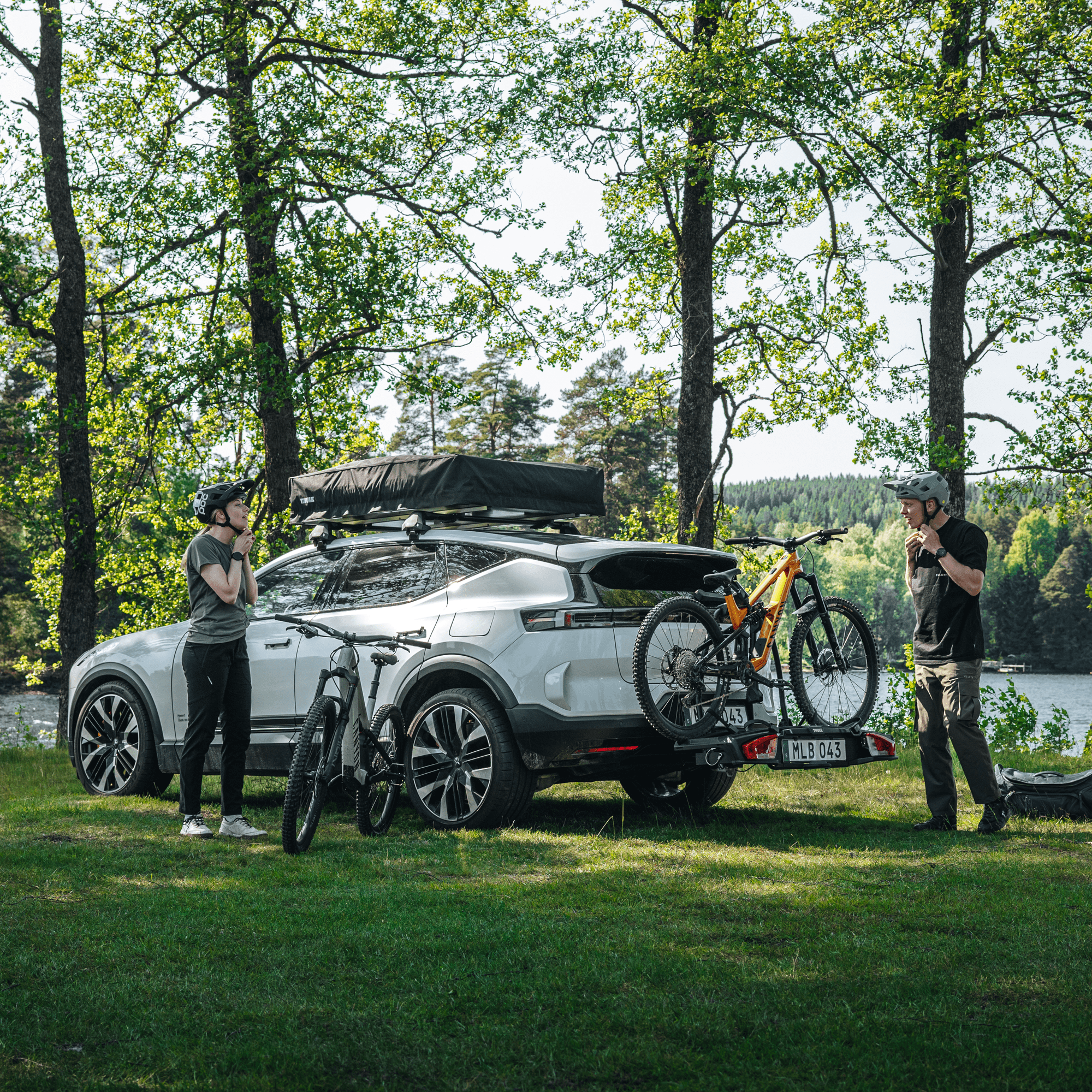 White SUV with a Thule VeloSpace 3 towbar bike rack carrying two mountain bikes, parked by a lake.
