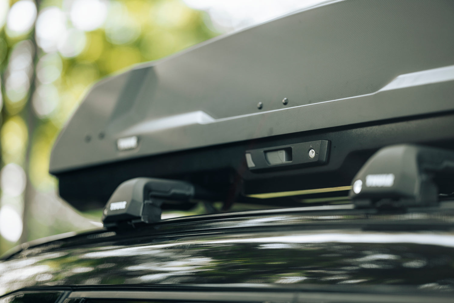 Close-up of a black Thule roof box mounted on a car, showing the latch mechanism and branding.