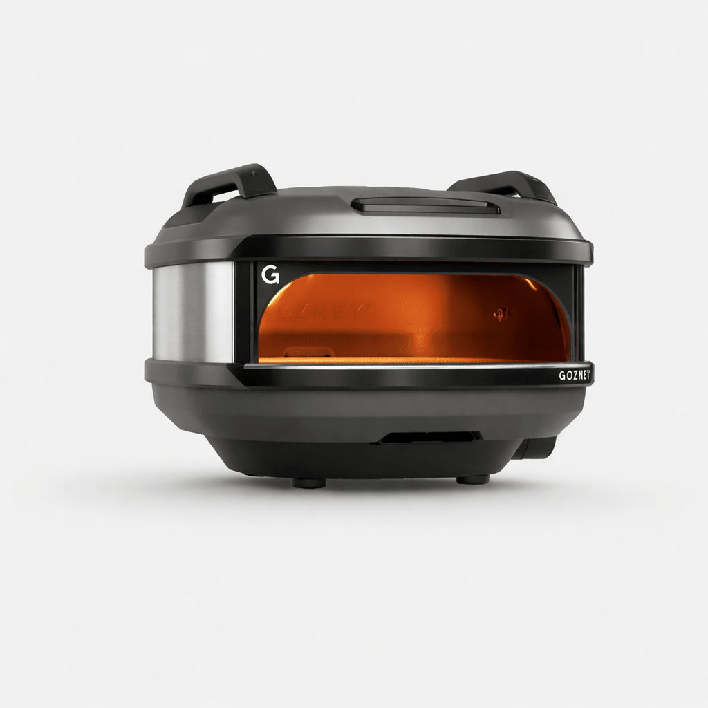 Compact black and silver Gozney Tread outdoor pizza oven with an orange-glowing interior.
