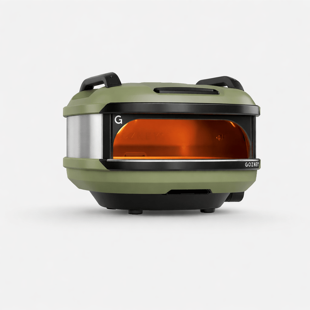 Compact Gozney Tread outdoor pizza oven in olive green with a silver band and glowing orange interior.