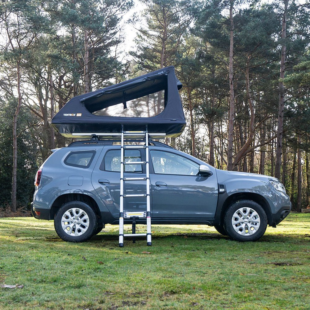 Black TentBox Go rooftop tent with ladder extended on a grey SUV in a forest.