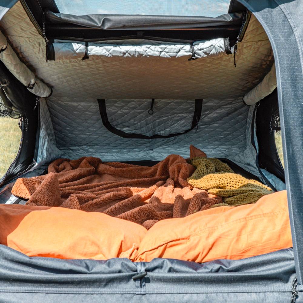 Interior view of a TentBox Go with a quilted silver thermal lining, orange pillows, and brown blankets.