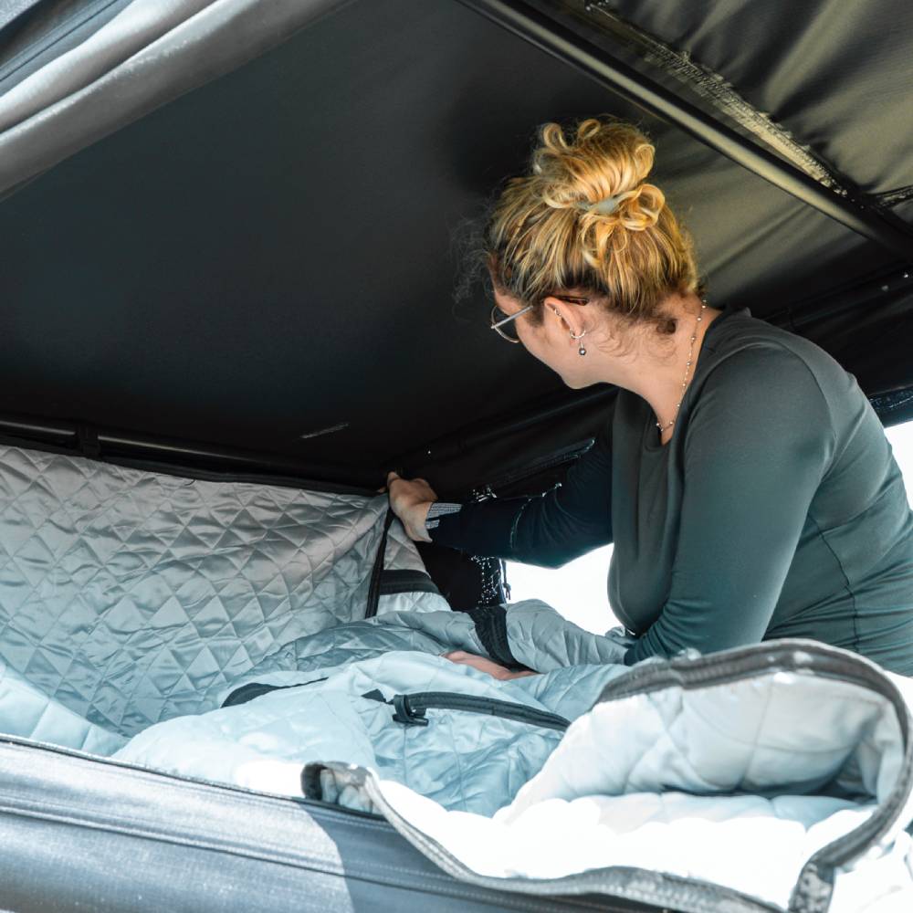 Woman installing a silver quilted TentBox Go Thermal Kit lining inside a black rooftop tent.