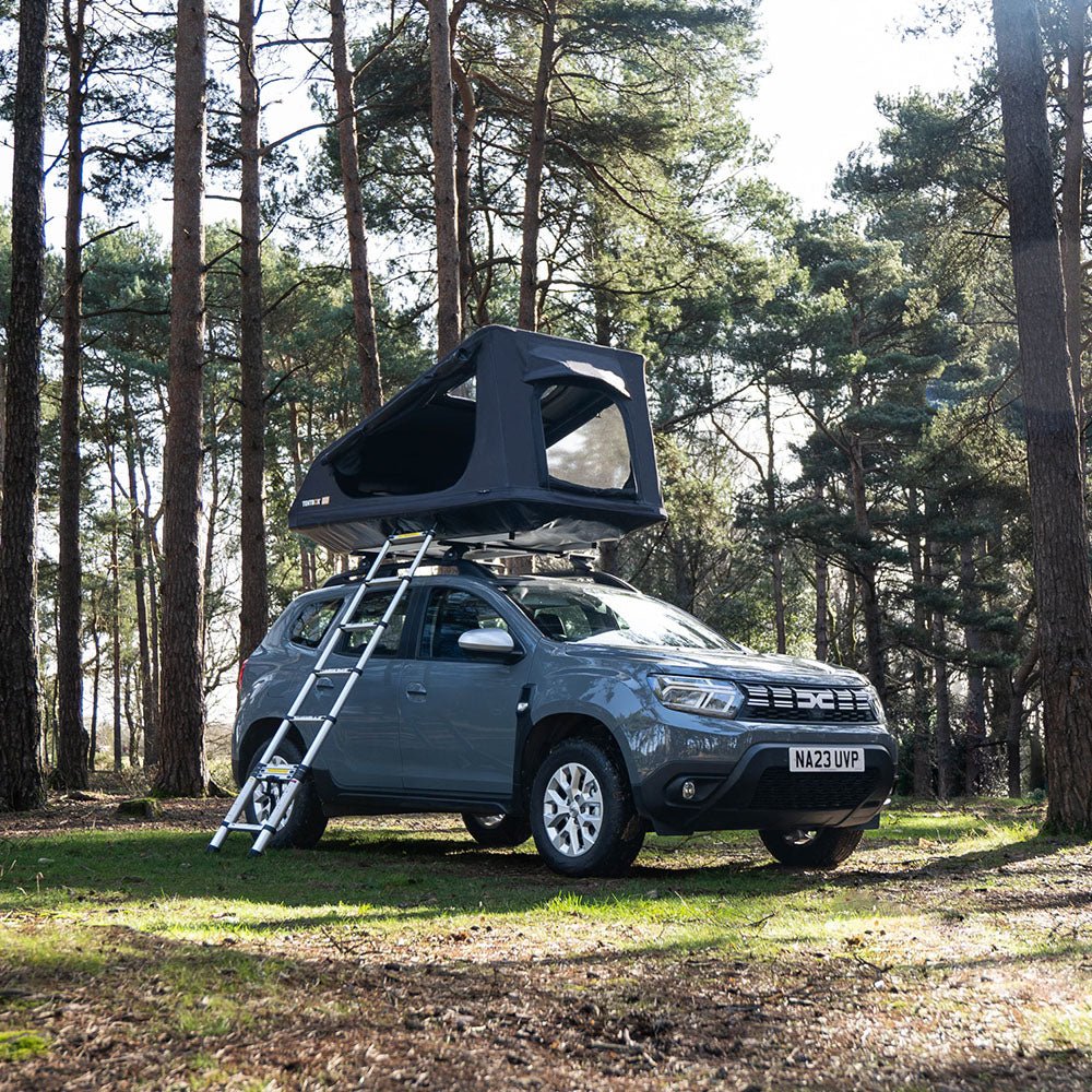 Dark grey TentBox Go rooftop tent with ladder on a grey SUV in a pine forest.
