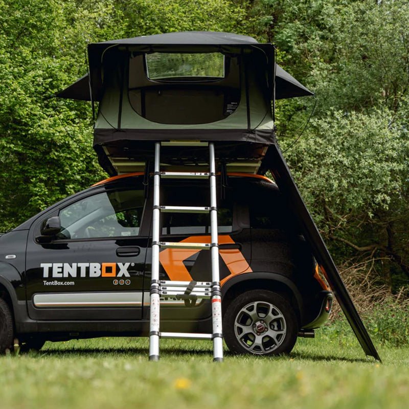 Black TentBox Lite roof tent with olive green windbreak attached, set up on a black car in a grassy area.