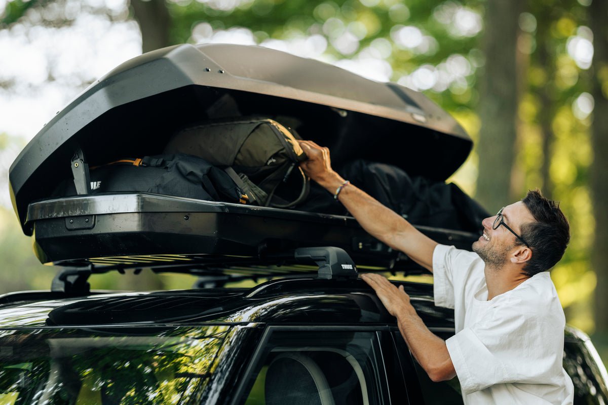 Lady opening a Thule roof box on top of her car with a forest background