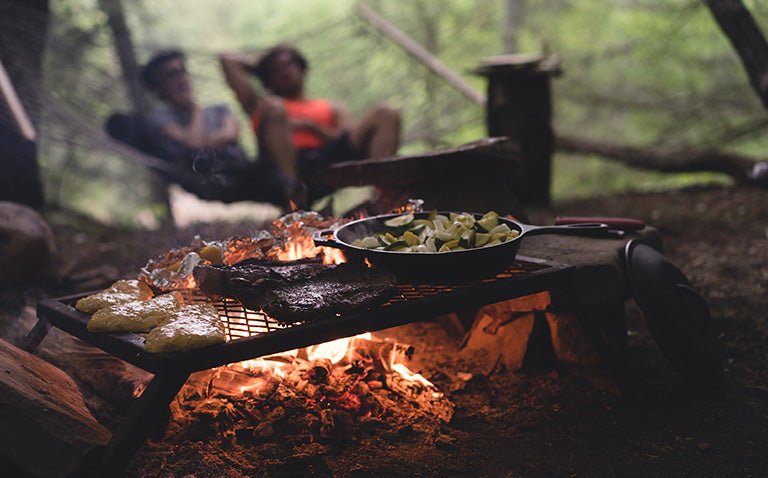 closeup of a camping grill with fire and steaks cooking on top