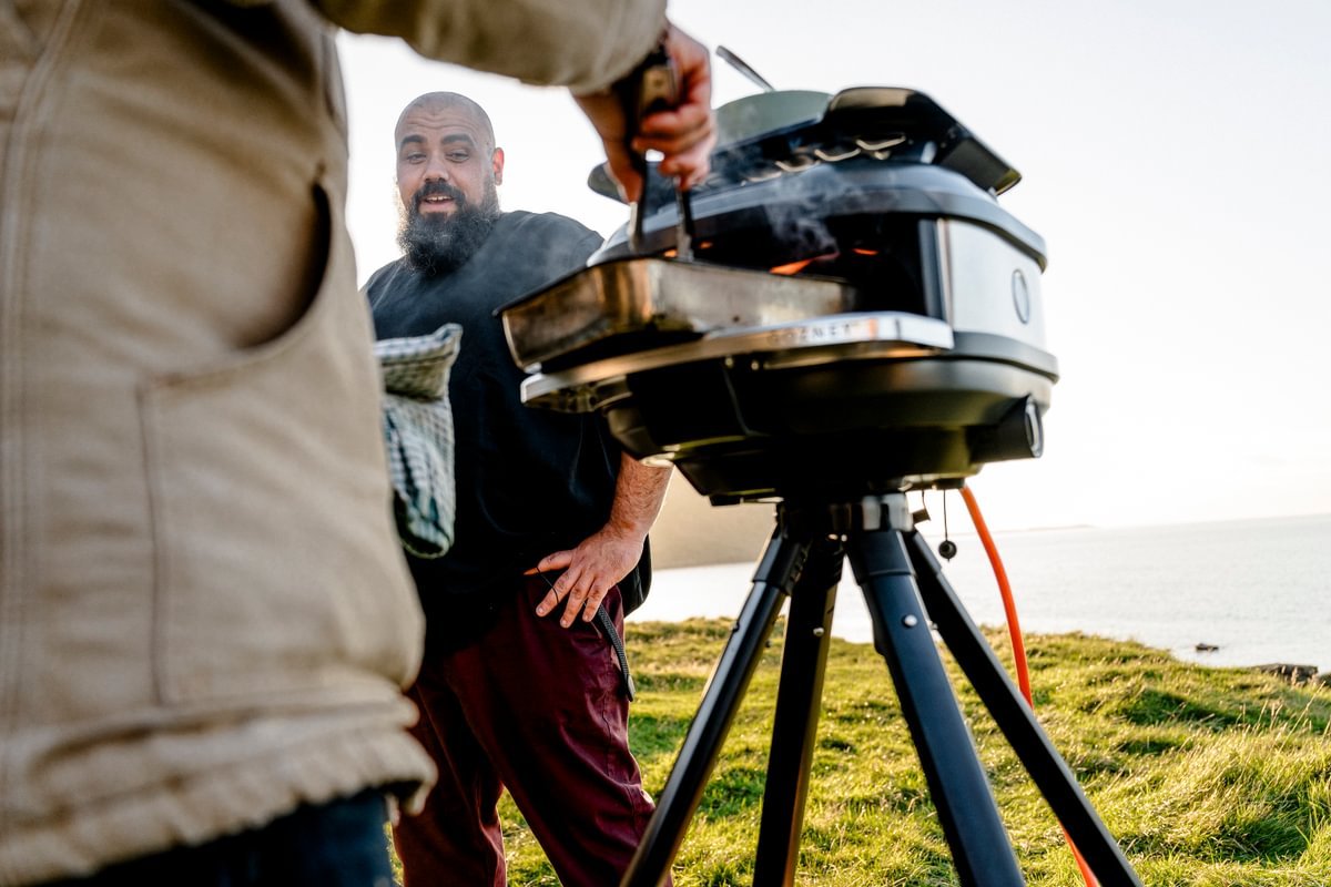 Two men in a field cooking with a Gozney Trea pizza oven