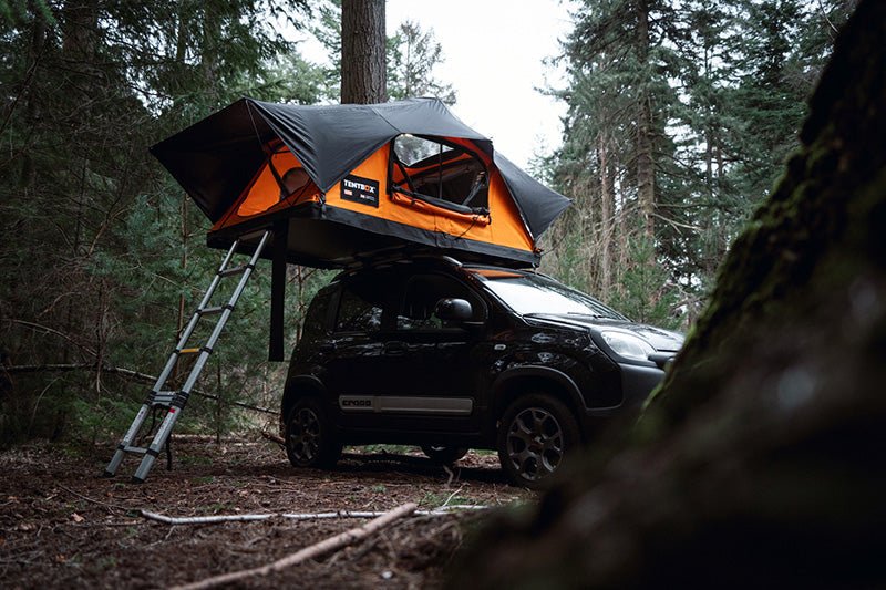 A car in a forest with an orange TentBox Lite XL on top