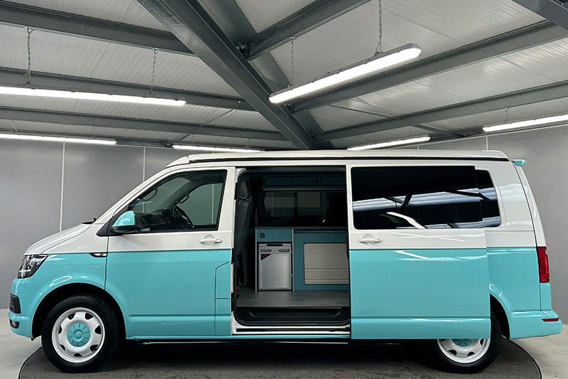 side profile of a two tone, blue and white VW campervan with painted blue wheels