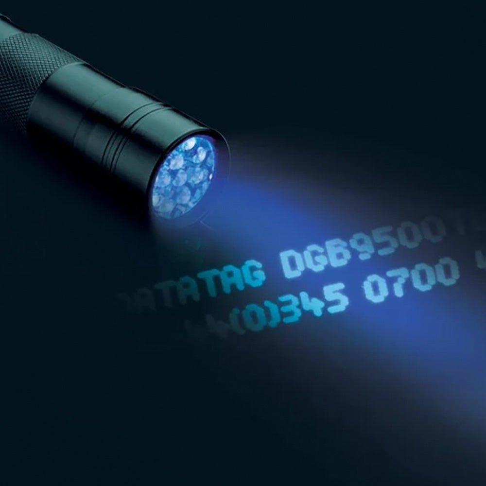 Black UV flashlight illuminating "DATATAG DGB9500" and numbers in bright blue on a dark surface.