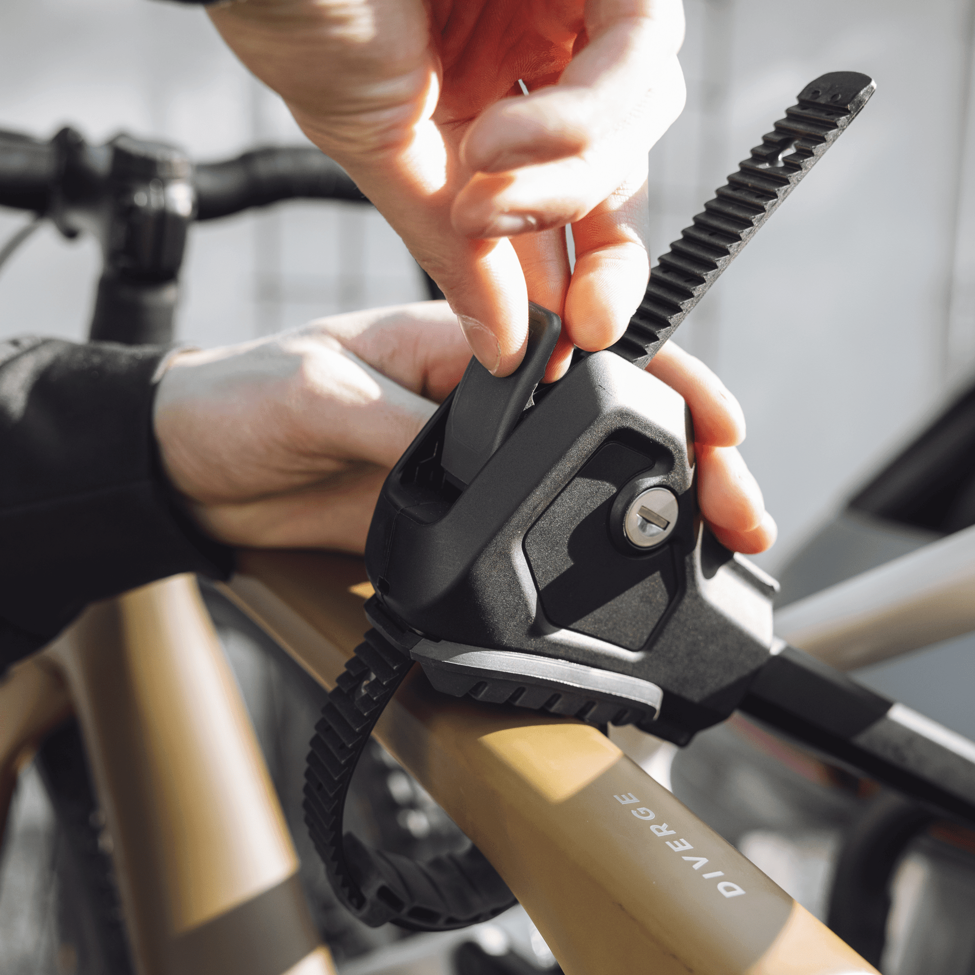 Hands securing a black Thule EasyFold 3 bike carrier strap onto a tan bike frame with a key lock visible.