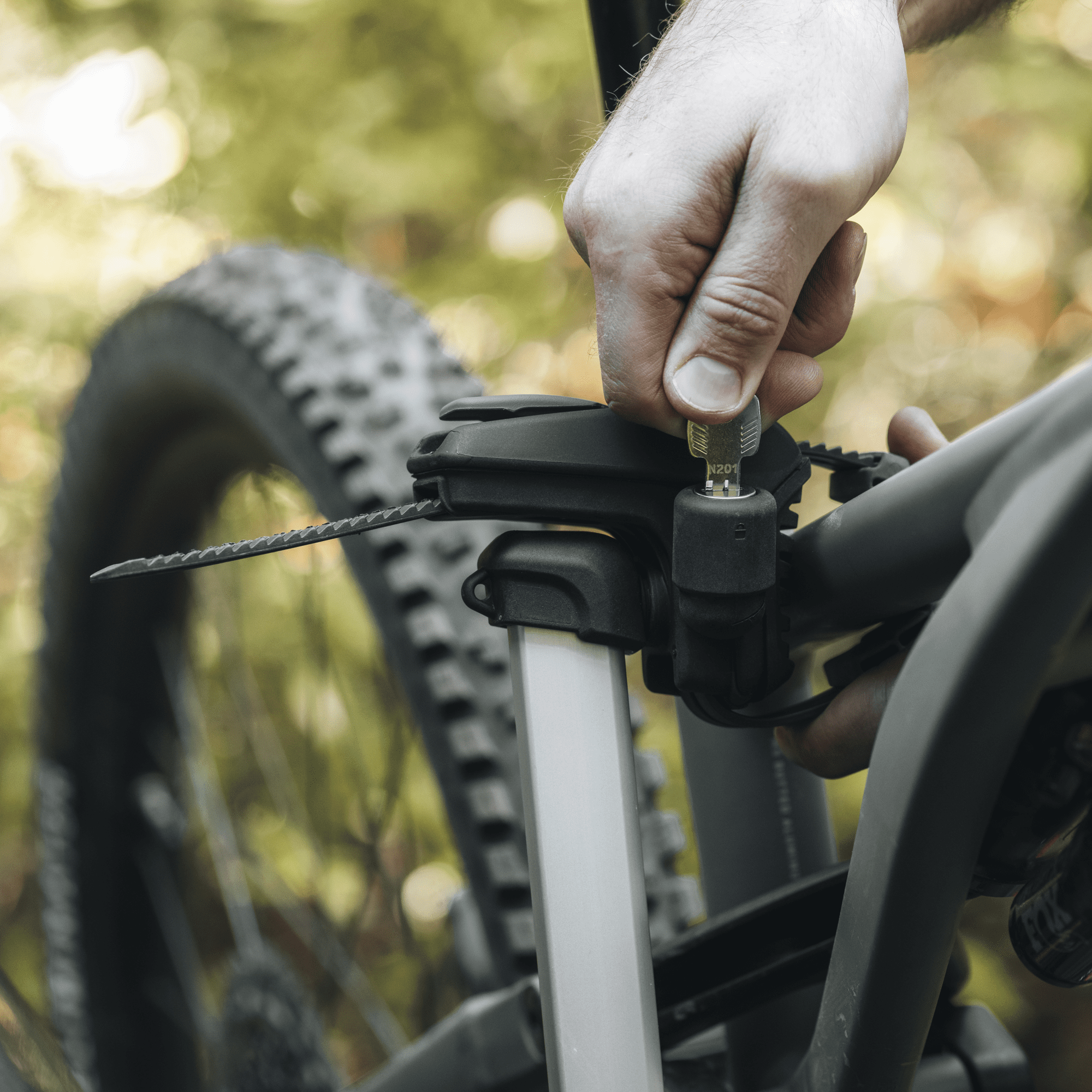 Hand securing a black Thule Epos 3-bike rack to a bicycle frame with a key, showing the silver support arm.