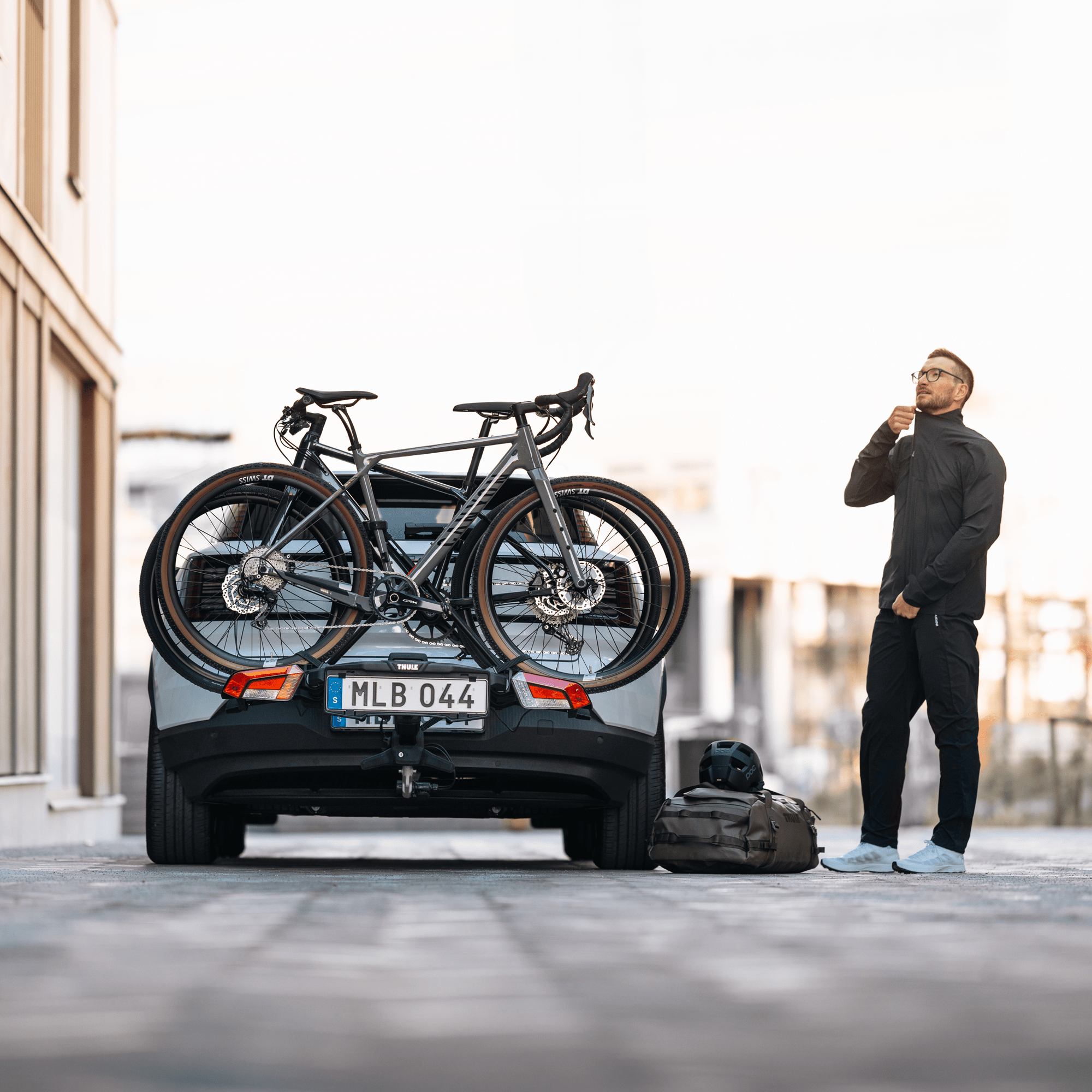 Thule OutPace 2-bike rack on a gray SUV, holding two dark gray bicycles. A man stands beside it.