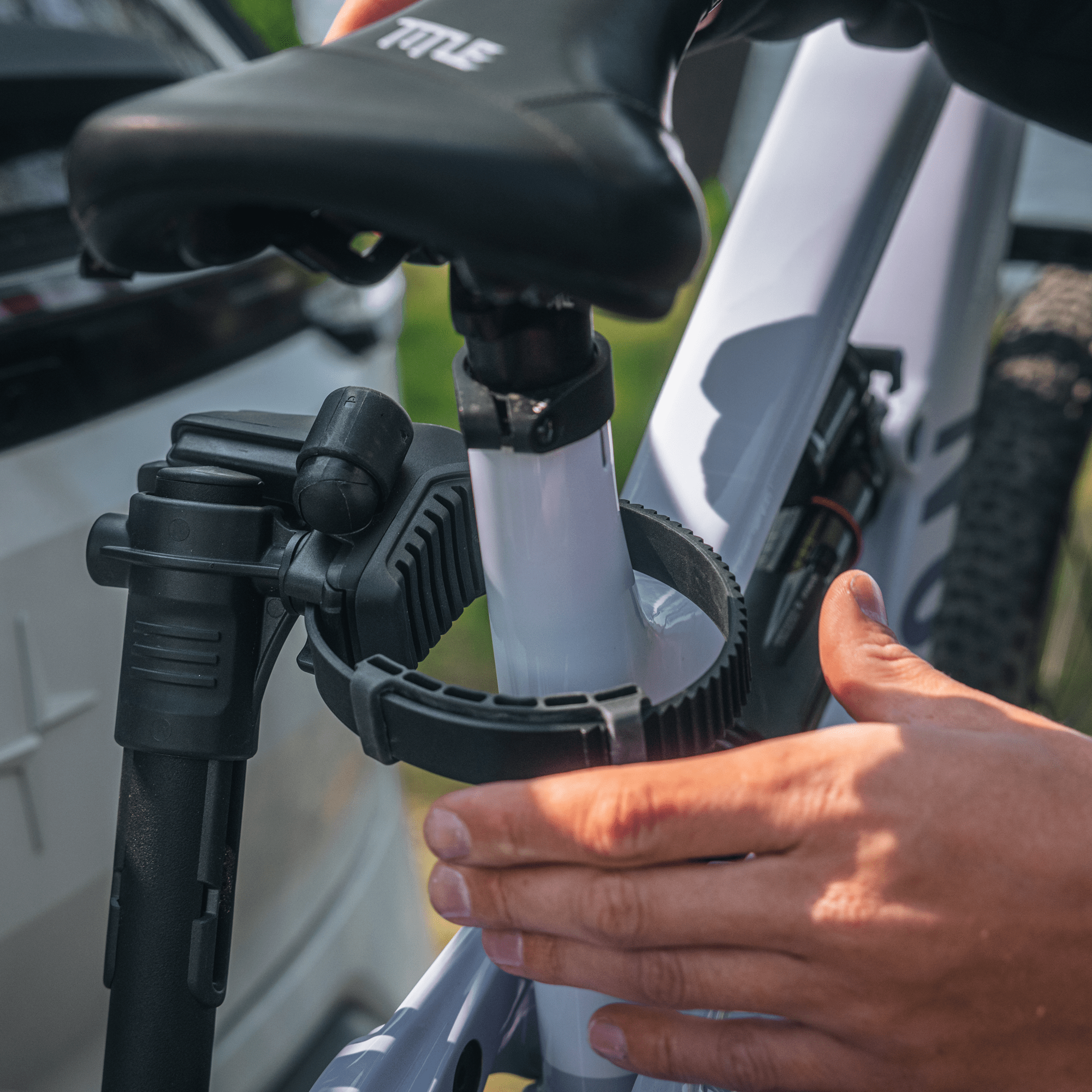 Hands securing a white bike frame to a black Thule VeloLite 1 platform bike carrier.