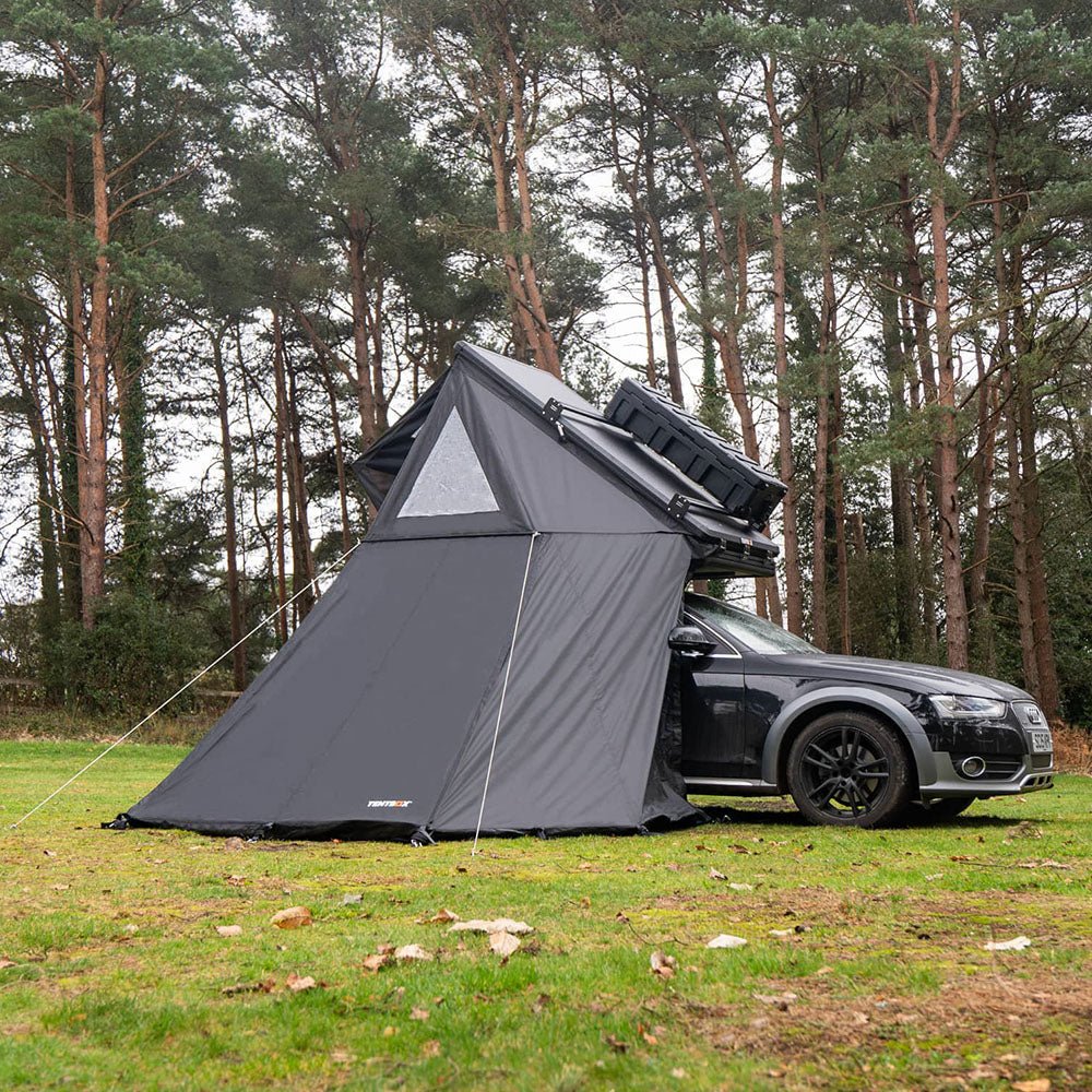 Black Cargo 2.0 Living Pod tent attached to a black Audi, set up in a forest clearing.