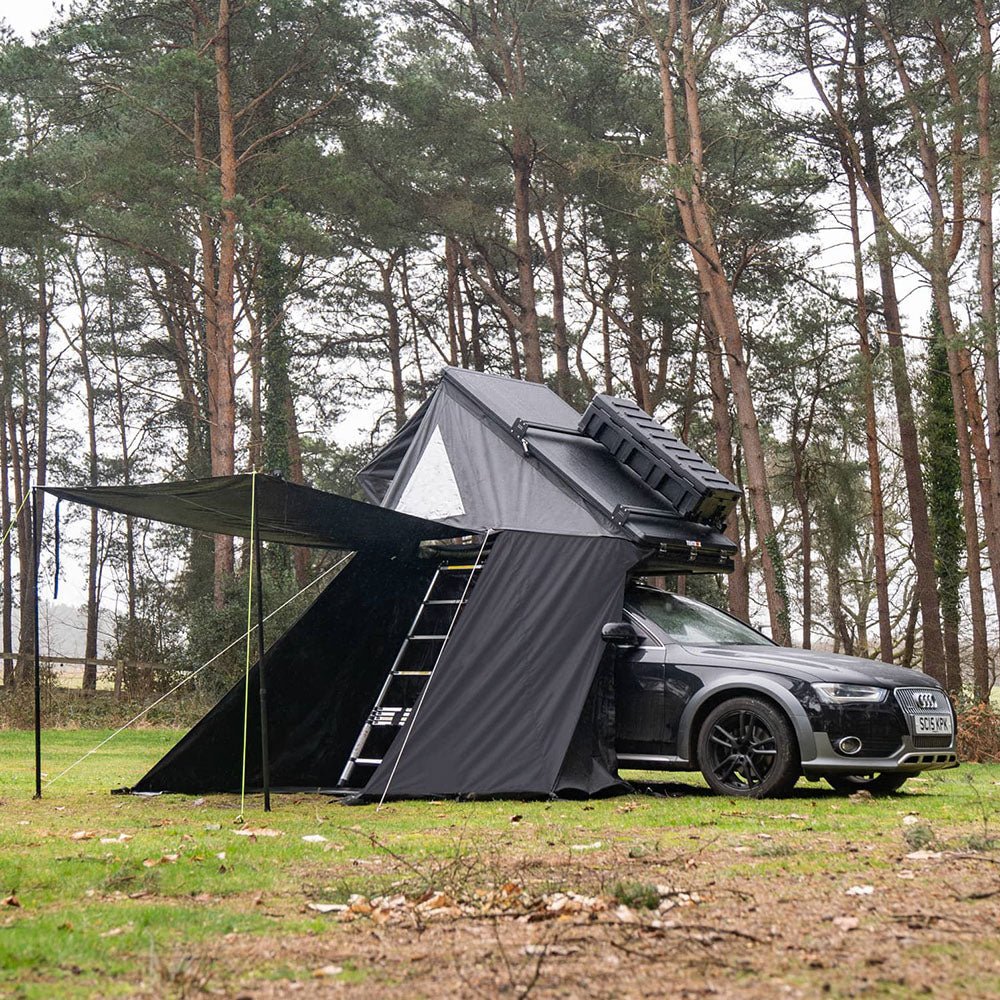Black TentBox Cargo 2.0 Living Pod attached to a car, creating a shaded area in a forest.